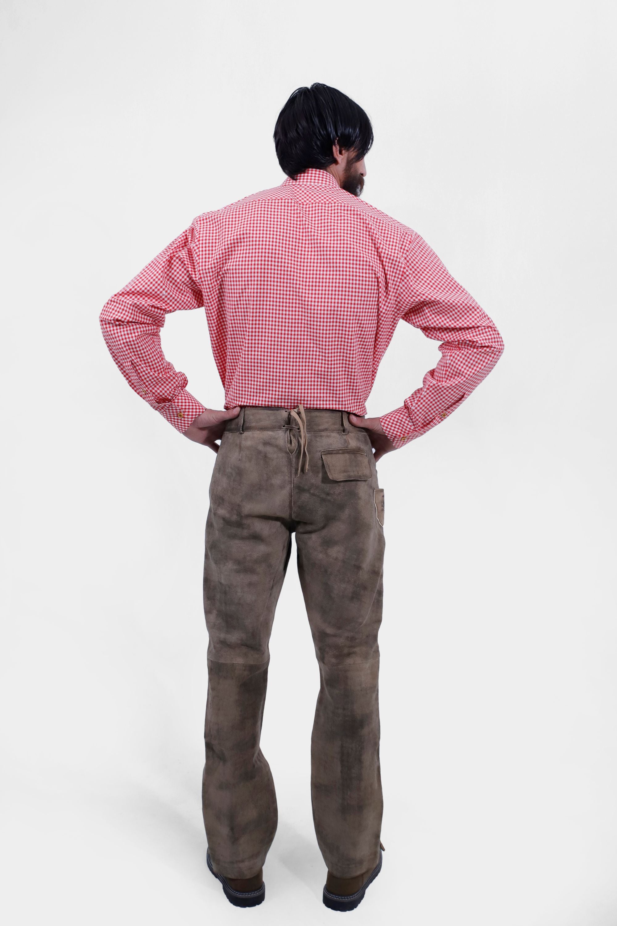 back view of a man wearing long lederhosen pants paired with red checkered shirt