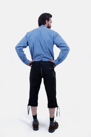 The man wearing the blue checkered shirt and black Bundhosen is shown from the back. The intricate detailing on the Bundhosen is visible, and he stands with his hands on his hips