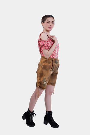 Side profile of the woman in Olivia Rodrigo Lederhosen, showing the adjustable waistband and laces on the leg cuffs, with a red checkered top.