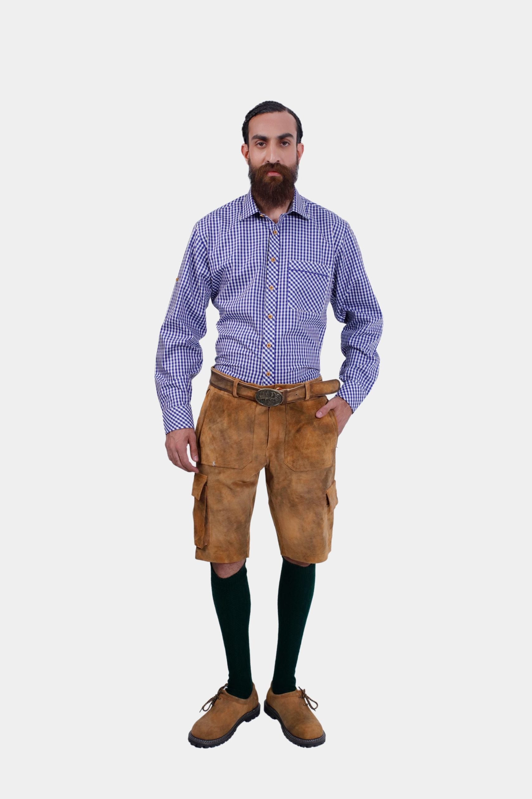 Full front view of a man wearing a blue and white checkered dress shirt and brown cargo lederhosen with pockets. He is standing with his left hand in his pocket, facing the camera.