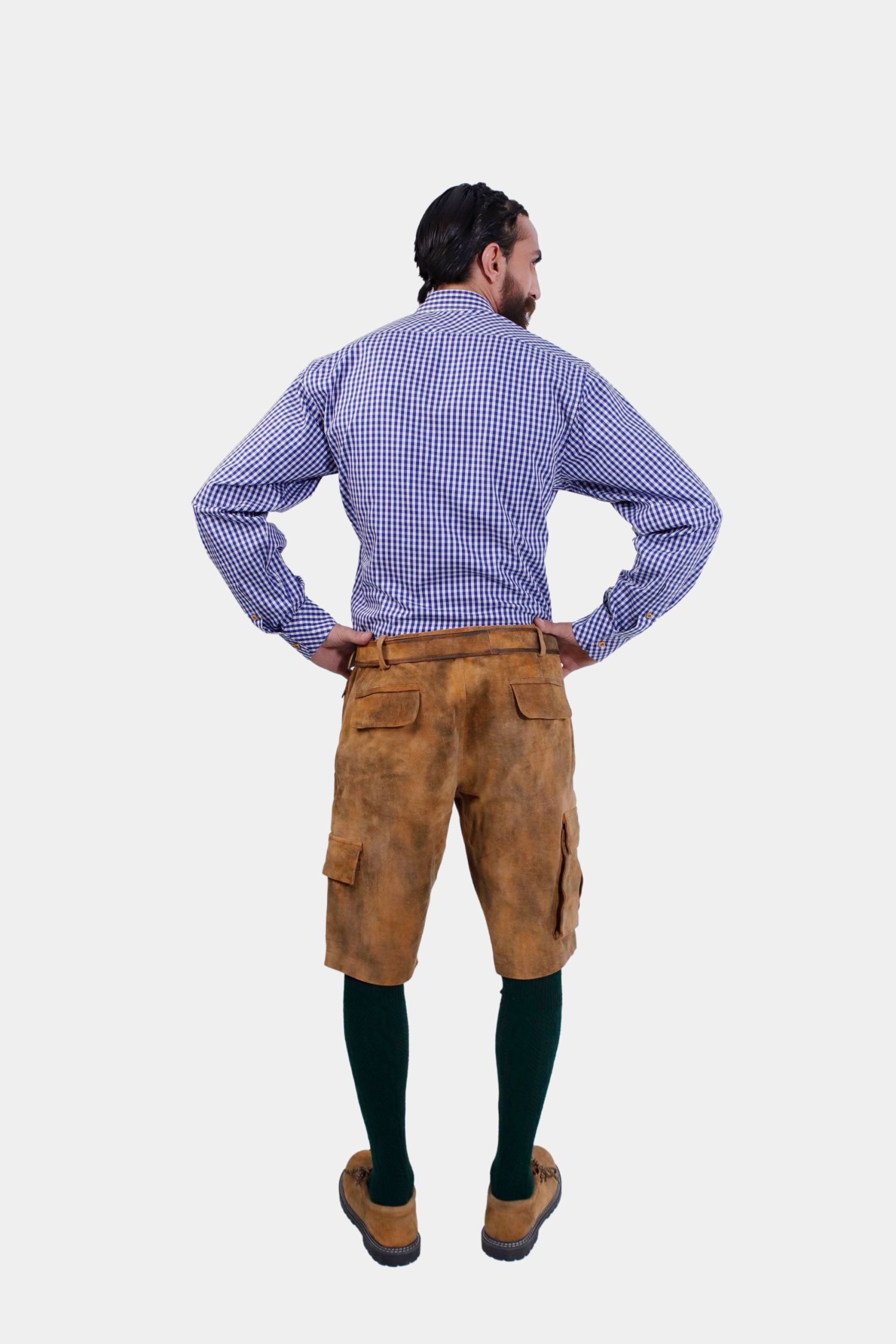 Back view of a man wearing a blue and white checkered dress shirt and brown cargo lederhosen. The back of the lederhosen features pockets, and he has his hands on his hips.