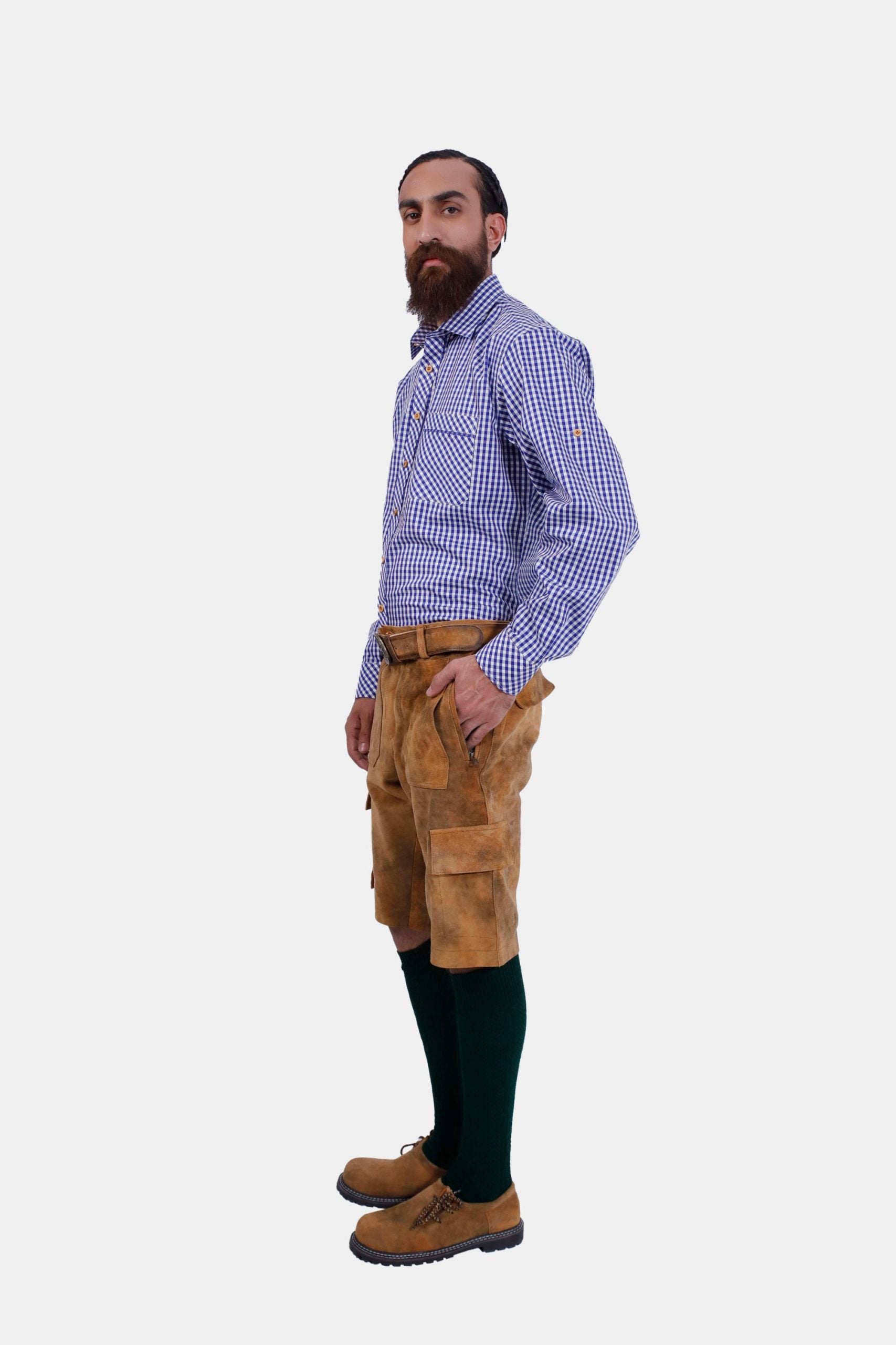 Side view of a man wearing a blue and white checkered dress shirt and brown cargo lederhosen, showing the pockets and belt detail. He has his left hand in his pocket and is looking slightly towards the camera.