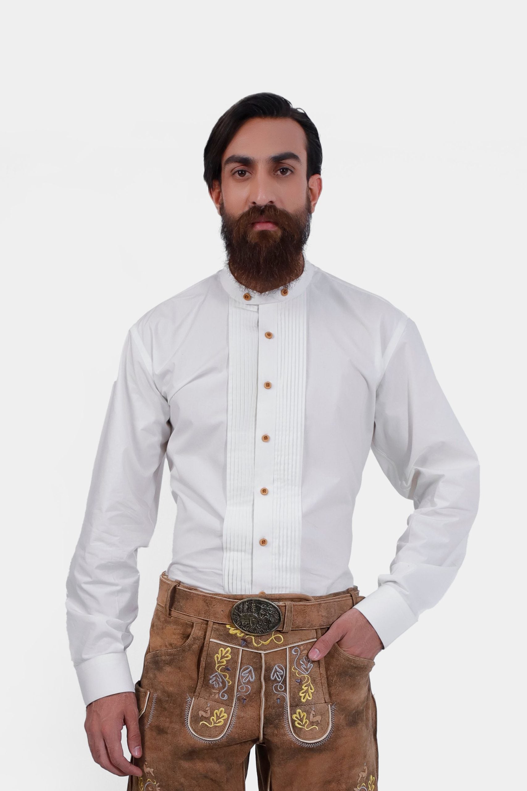 A man wearing the Rainer Bock Lederhosen Shirt, a white long-sleeve shirt with a tuxedo front, pleats, and wooden buttons. He pairs it with light brown embroidered Lederhosen, perfect for Oktoberfest.