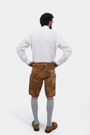 Rear view of a man wearing a white dress shirt and tan leather lederhosen shorts, showing the back pockets and overall fit of the lederhosen along with grey knee-high socks.