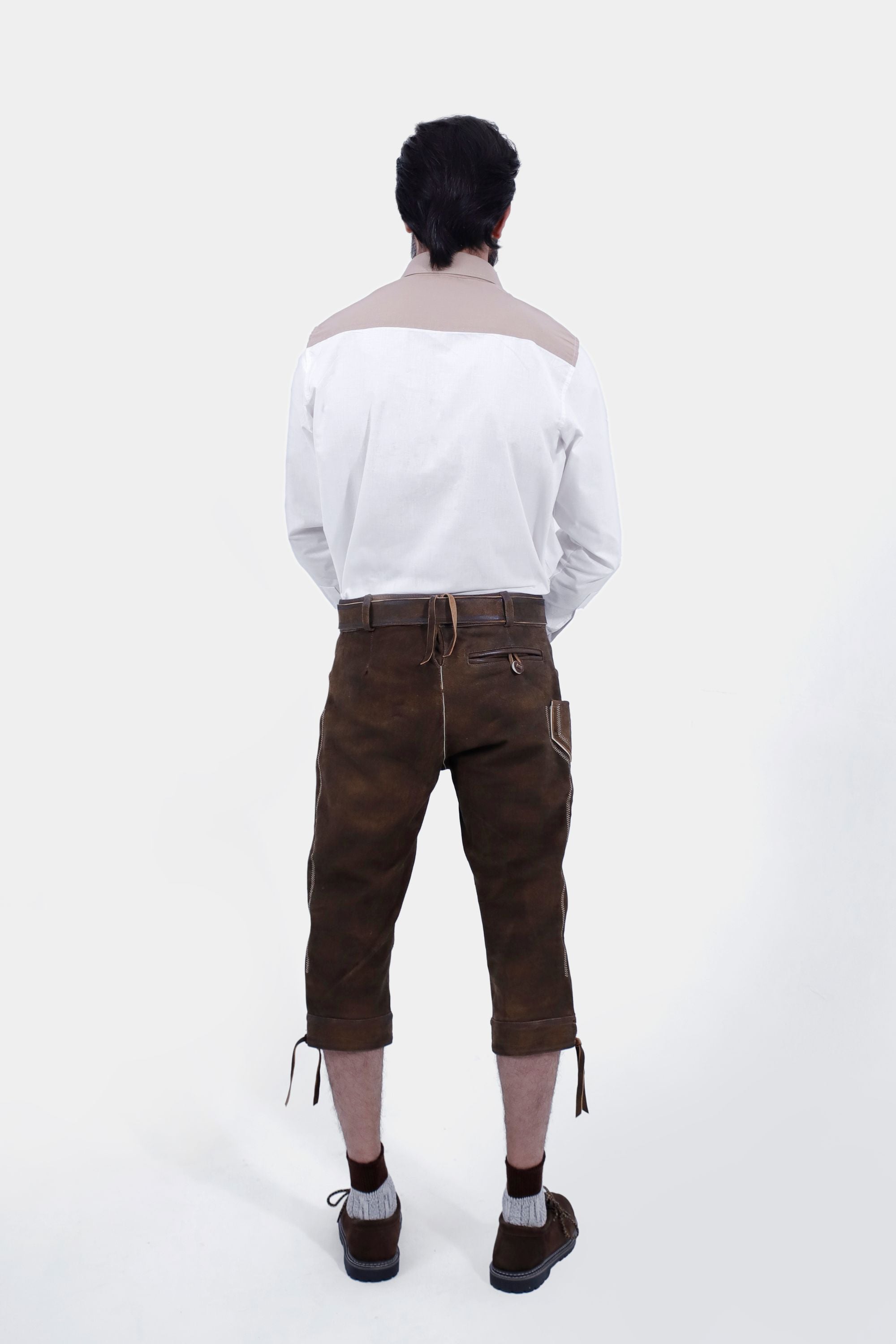 Rear view of a man wearing a white shirt with brown accents and brown leather bundhosen, showing the back pockets and overall fit of the bundhosen.