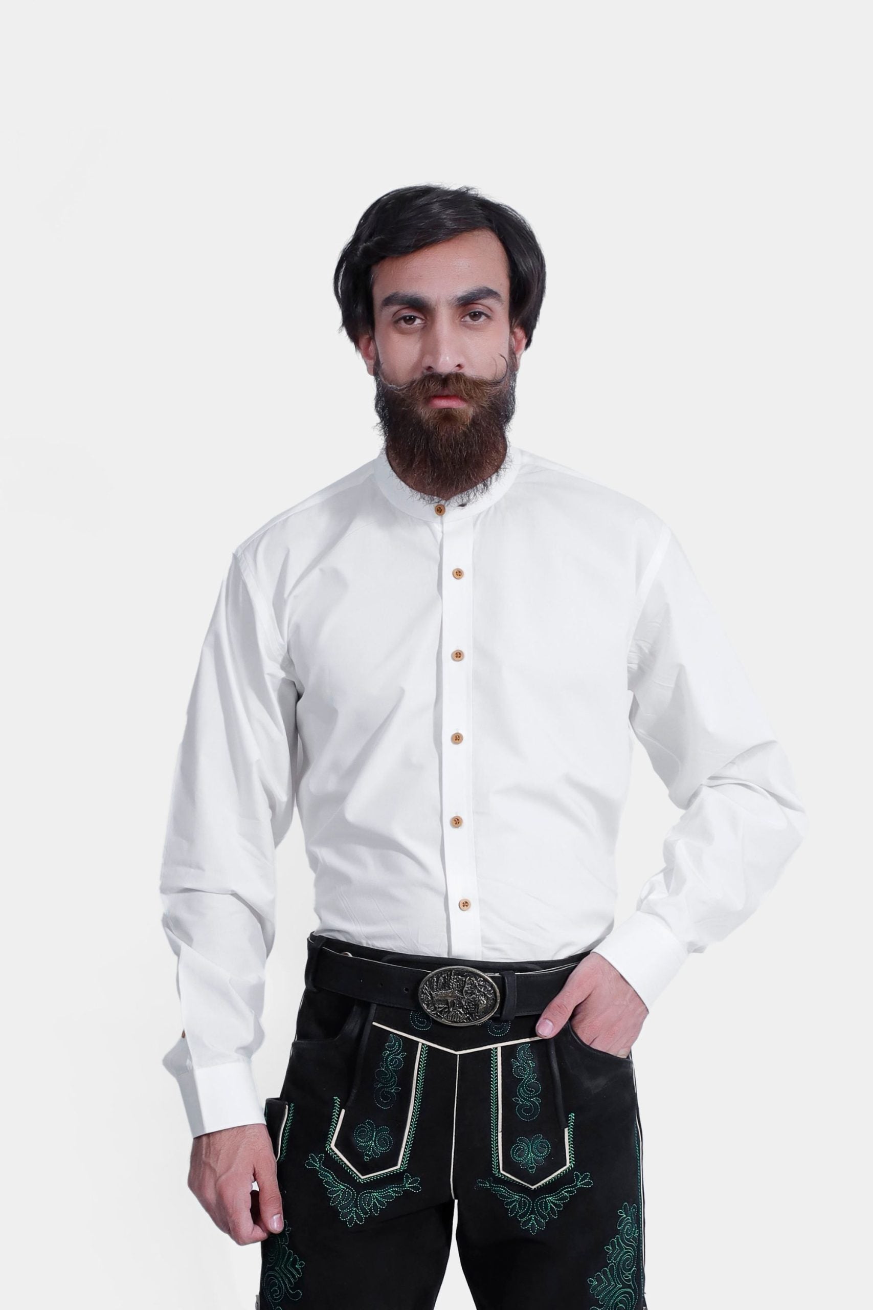 A man wearing the Ryan Lederhosen Shirt, a traditional white long-sleeve shirt with a mandarin collar and wooden buttons. He pairs it with black leather Lederhosen adorned with green embroidery and a decorative belt buckle. This ensemble is ideal for Oktoberfest and other Bavarian cultural events.
