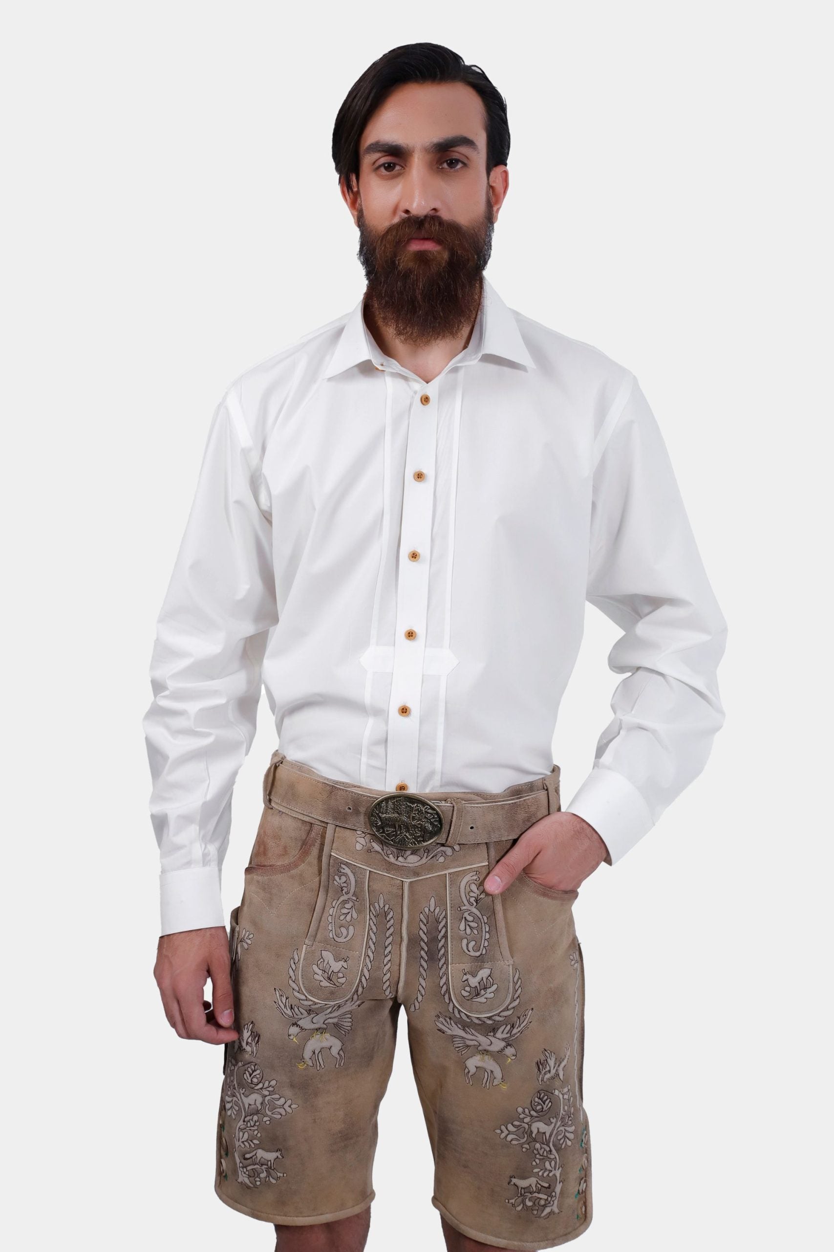 Front view of the man standing with one hand in his pocket, showcasing the detailed embroidery on the beige Lederhosen and the traditional white shirt.
