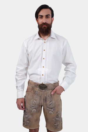 Front view of the man standing with one hand in his pocket, showcasing the detailed embroidery on the beige Lederhosen and the traditional white shirt.