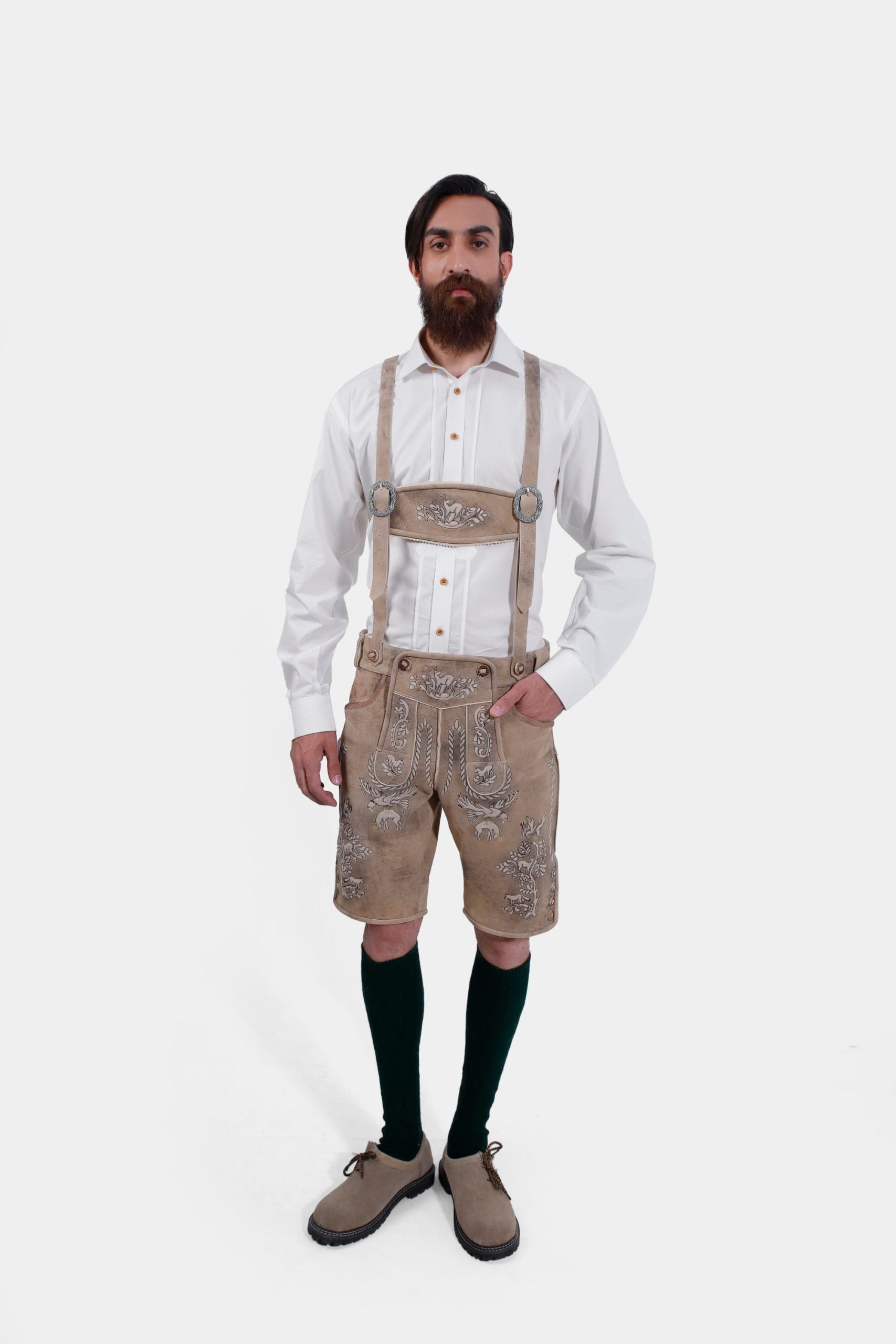 Full body shot of the man wearing the white shirt and beige Lederhosen, with green knee-high socks and beige shoes. He also has traditional suspenders attached to the Lederhosen.