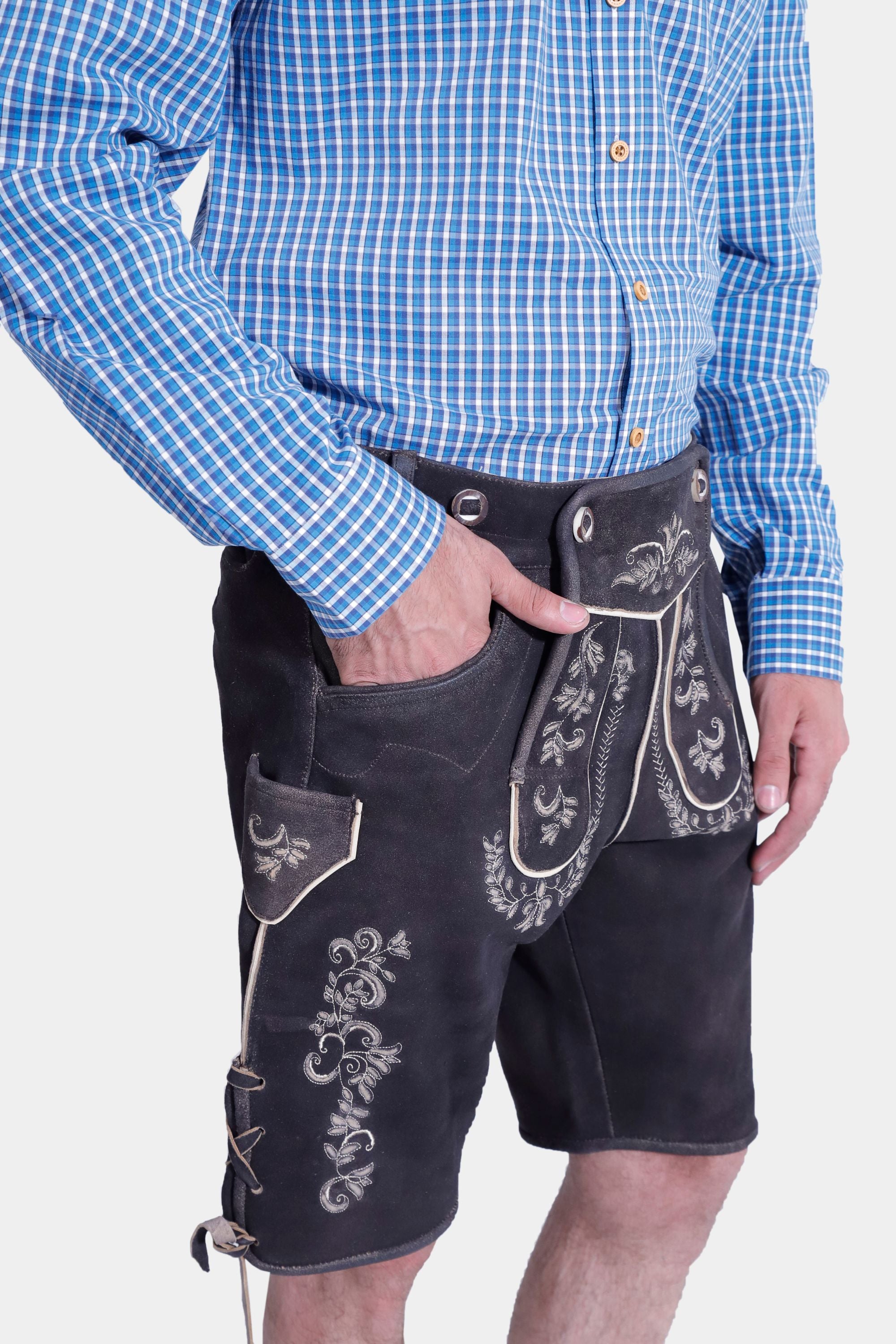 Side view of a man in the Gert Fröbe Lederhosen Outfit, showcasing the intricate embroidery on the black leather shorts and the blue checkered shirt."