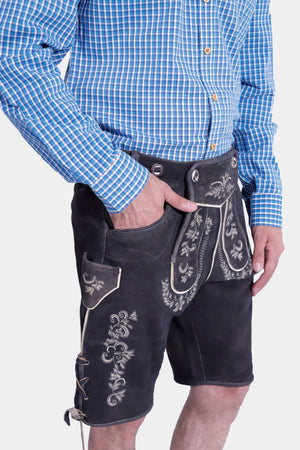 Side view of a man in the Gert Fröbe Lederhosen Outfit, showcasing the intricate embroidery on the black leather shorts and the blue checkered shirt."