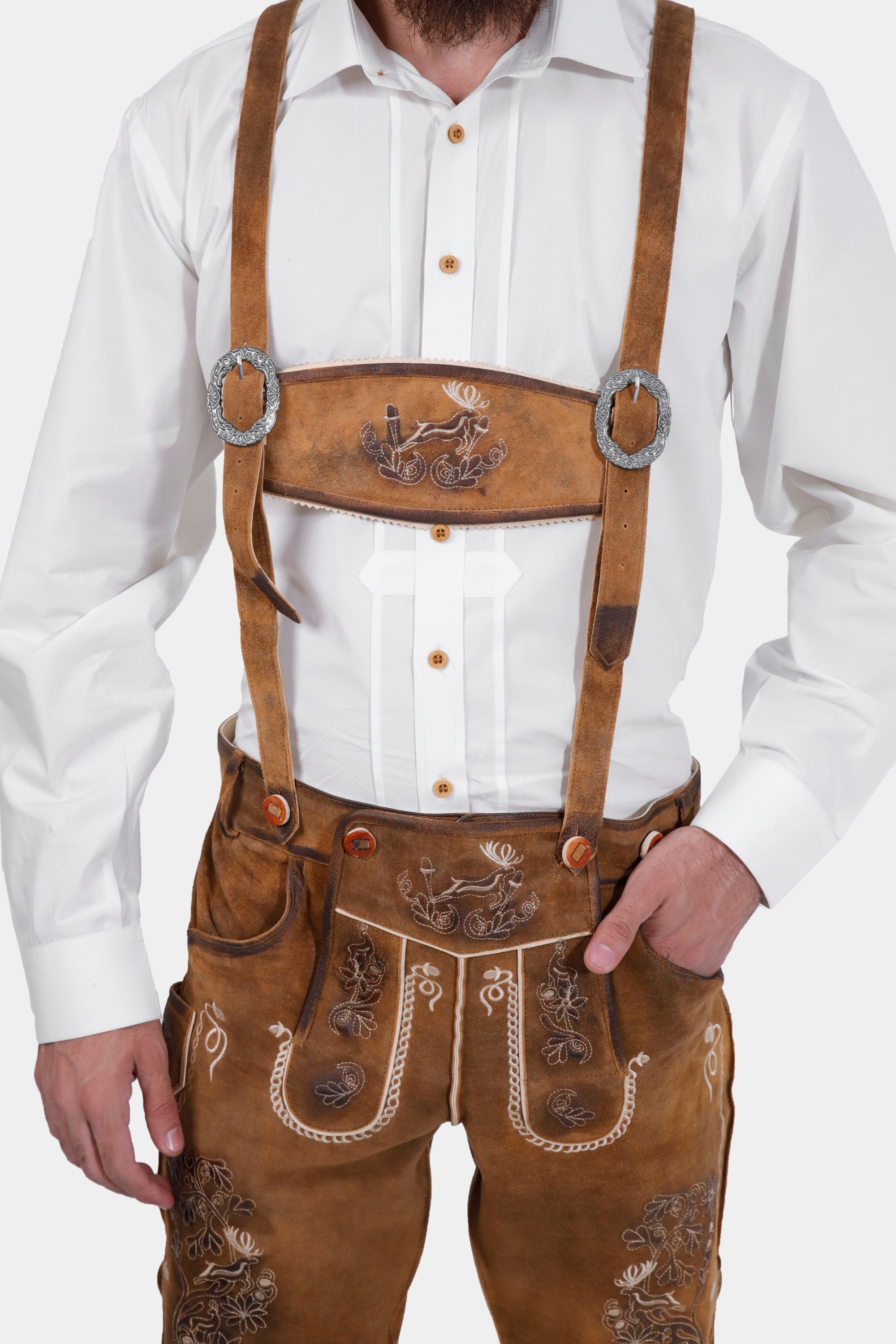 Close-up of a man wearing a white dress shirt and brown lederhosen with suspenders. The suspenders feature decorative embroidery, including a deer motif on the front strap.