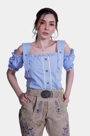 Close-up of a woman wearing a blue checkered blouse and beige Lederhosen shorts, showcasing the embroidery details on the shorts.