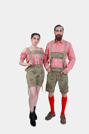 A couple dressed in traditional Volksfest outfits. The woman is wearing a red checkered off-shoulder top with a pair of green leather shorts featuring intricate embroidery. The man is wearing a matching red checkered shirt with green leather shorts, also decorated with detailed embroidery. Both outfits include suspenders, and the man is wearing red knee-high socks with brown shoes while the woman is in black lace-up boots.