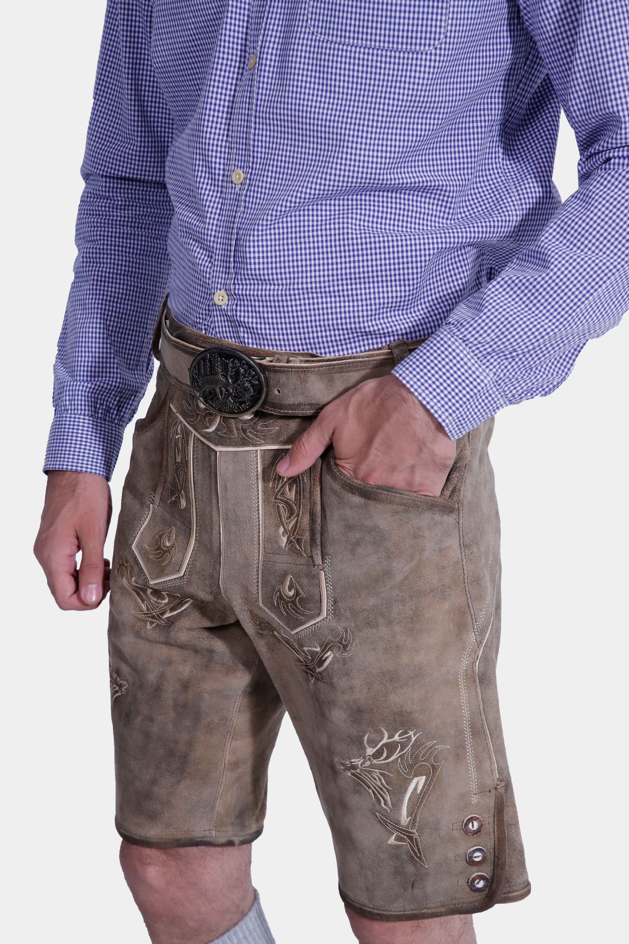 A close-up of a man wearing Stonewashed Fawn Lederhosen with intricate natural-colored embroidery, paired with a blue checkered shirt. The focus is on the embroidery and the belt buckle.