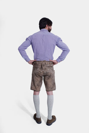 A rear view of a man wearing Stonewashed Fawn Lederhosen, highlighting the back pocket and embroidery. He is also wearing a blue checkered shirt, light grey knee-length socks, and brown shoes.