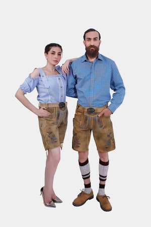 A couple dressed in matching Wiesn outfits with intricately embroidered Lederhosen shorts, posing together. The man wears a blue checkered shirt, and the woman sports an off-shoulder blouse, both exuding Bavarian charm.