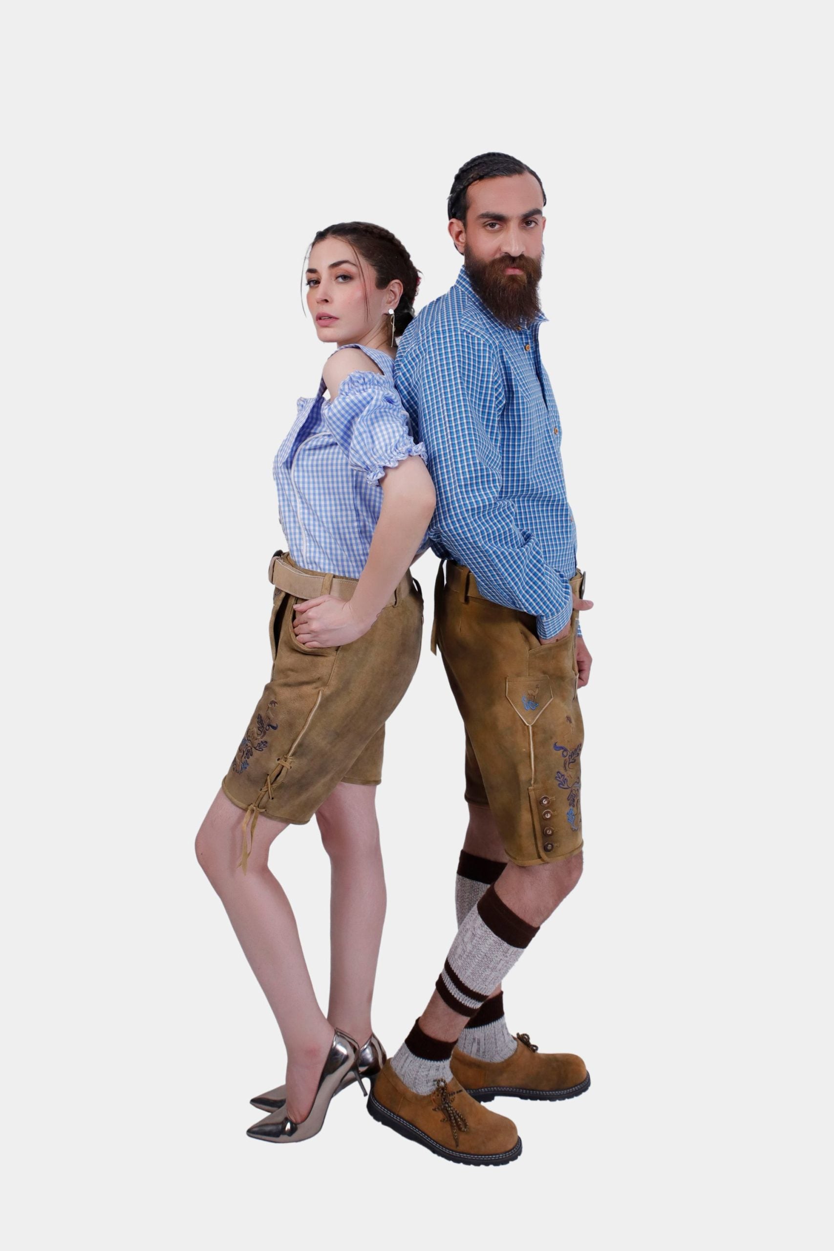 A couple wearing matching Wiesn outfits with intricately embroidered Lederhosen shorts, posing back to back. The man is dressed in a blue checkered shirt, and the woman is in a stylish off-shoulder blouse."