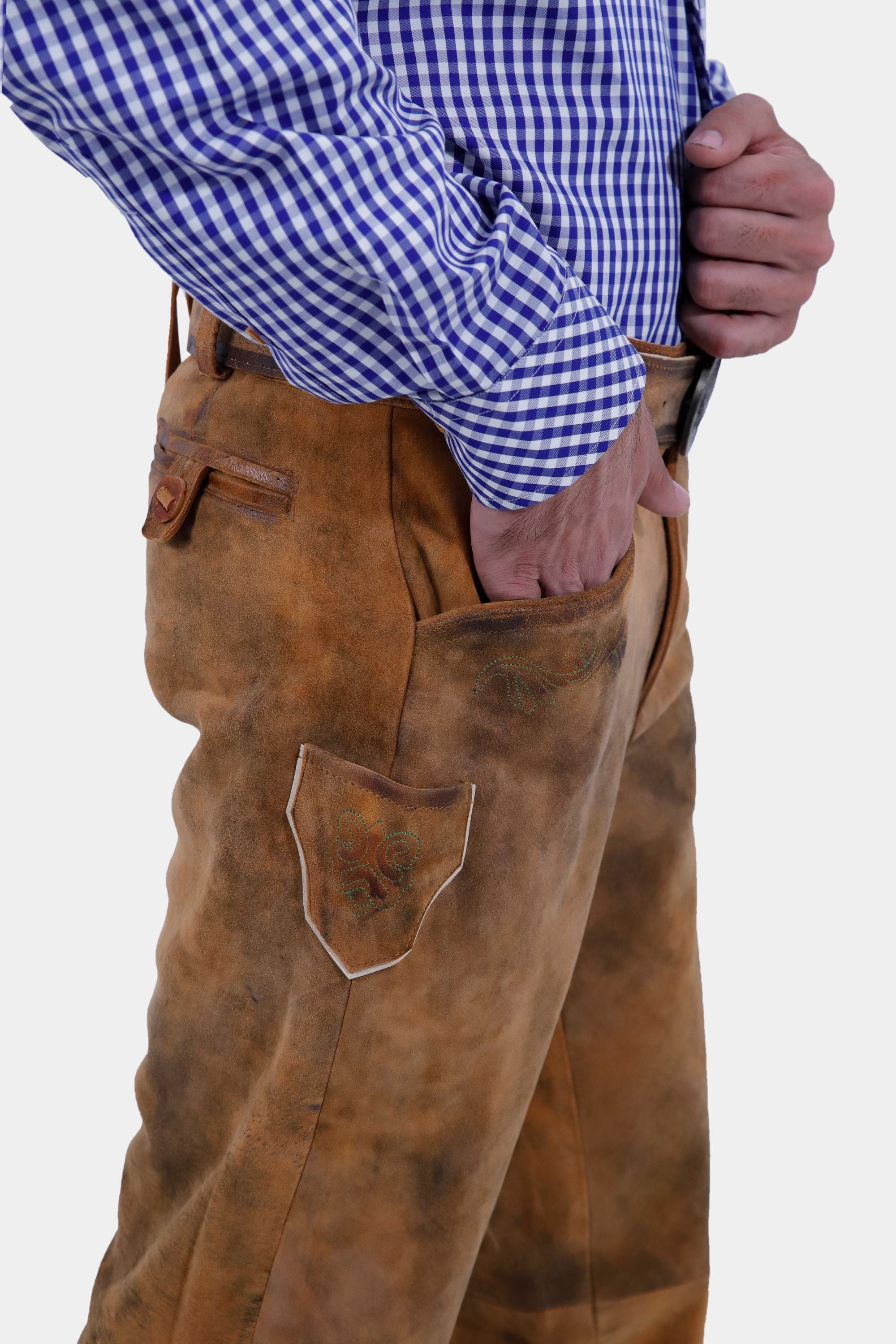 Close-up of a bearded man wearing a blue and white checkered shirt and brown leather long lederhosen. He has one hand in his pocket, highlighting the intricate details and texture of the lederhosen.