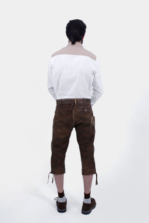 Rear view of a man wearing a white shirt with brown accents and brown leather bundhosen, showing the back pockets and overall fit of the bundhosen.