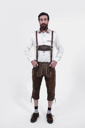 A man wearing earthy brown leather Zwiesel Suspenders with intricate Bavarian embroidery and circular metal clasps, paired with a white shirt, matching Zwiesel Bundhosen, brown shoes, and socks.