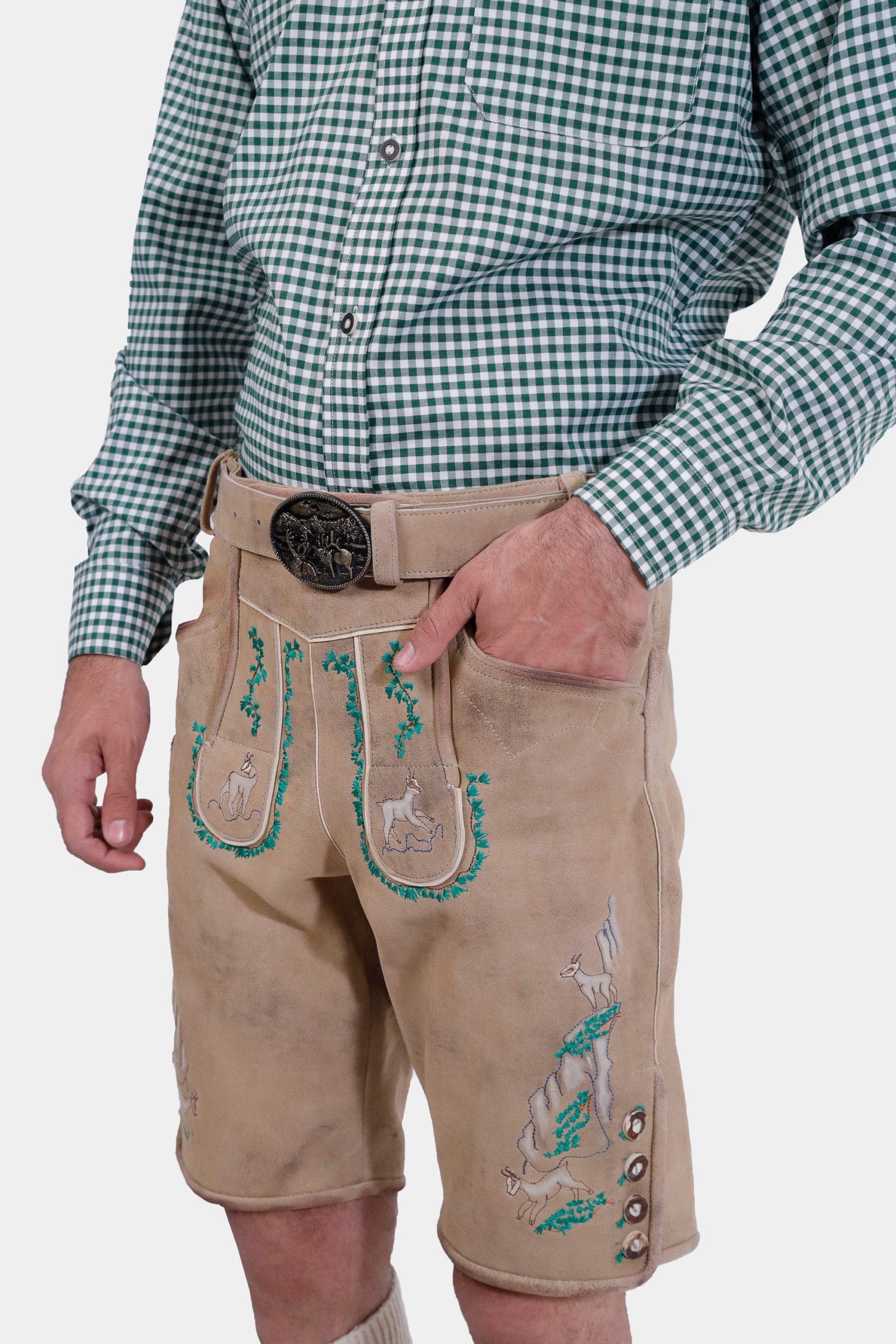 Close-up of a man's waist showing beige lederhosen with green embroidery and a traditional belt buckle, with his hand in the pocket.