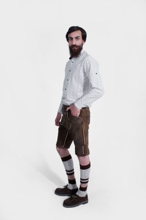 Side view of a man wearing traditional Bavarian Lederhosen. The outfit includes a white shirt with a subtle pattern and brown leather shorts with intricate embroidery. He completes the look with knee-high woolen socks and brown shoes. The attire captures the classic Bavarian style.
