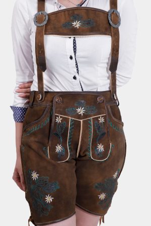 A close-up of a woman wearing earthy brown leather lederhosen with intricate green and white floral embroidery, paired with a white shirt and suspenders.