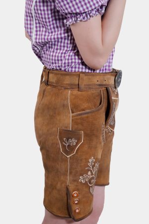 Side view of a model in brown leather lederhosen shorts with white embroidery, showcasing the side pocket and button detailing, paired with a purple checkered blouse