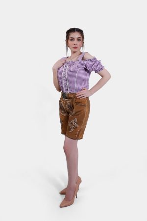 Model striking a pose in brown leather lederhosen shorts with white embroidery, paired with a purple checkered blouse and nude high heels, seen from the side.