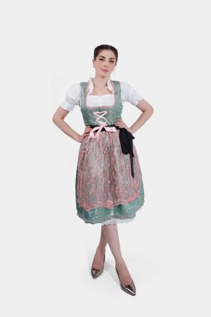 A full-length shot of the woman in the green and pink dirndl, standing with her hands on her hips. She is wearing metallic pointed heels, completing the traditional yet stylish look.