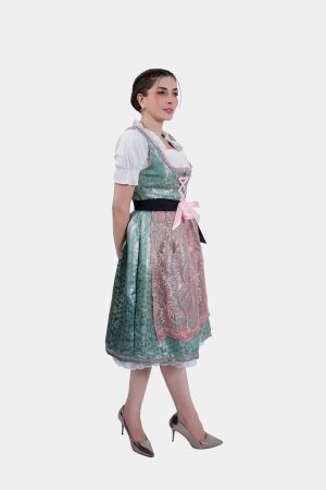 A side profile of the woman wearing the dirndl, looking over her shoulder. The green and pink colors of the dirndl stand out against the white background, with the black ribbon accentuating her waist.