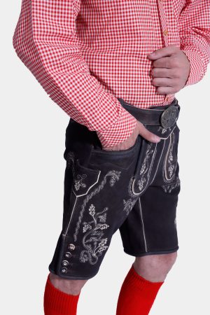 Side view of a man wearing black Lahm Lederhosen with intricate white embroidery, paired with a red checkered shirt and red knee-high socks, highlighting the detailed side panel and pocket design.