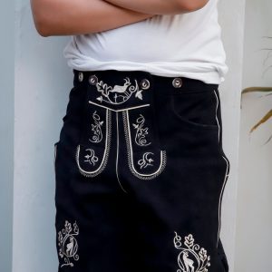 Close-up of a young boy in a white t-shirt wearing 'Bernd Leno Lederhosen' in black, showcasing detailed white embroidery on the bib and pockets, standing with arms crossed.