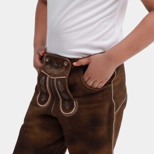 Close-up of a young boy in a white T-shirt wearing traditional brown Elias Lederhosen with detailed embroidery on the bib, standing with hands in pockets.