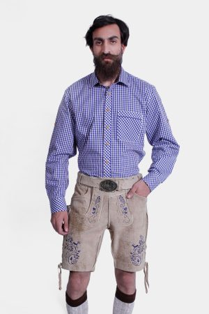 Man standing in a beige Lederhosen outfit with blue floral embroidery, paired with a blue and white checkered shirt and rustic socks.